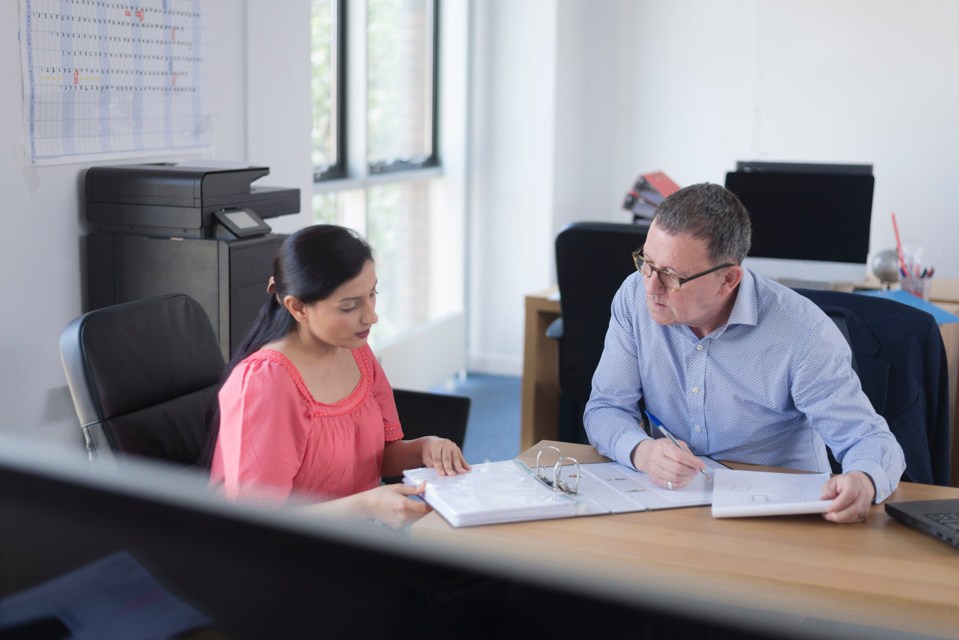 Professional advisor explaining personalized financial plan details to attentive client with charts and graphs visible