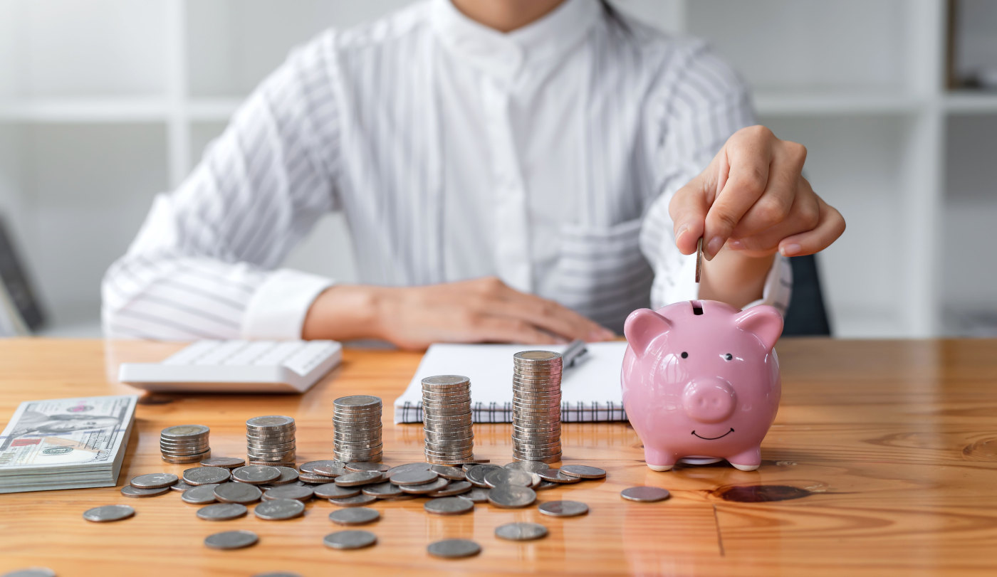 Close-up of hand inserting coin into piggy bank symbolizing the importance of consistent savings and financial discipline